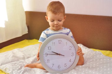 Yatağa yatmadan önce oturan büyük bir yuvarlak saat tutan şirin yürümeye başlayan çocuk