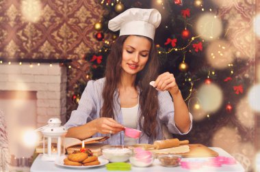 Genç güzel kadın bir aşçının şapkalı Noel kurabiyeleri Noel ağacı arka planda hazırlanıyor