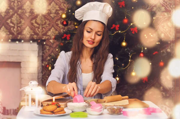 Young beautiful woman in a cook\'s hat preparing Christmas cookies in the background of the Christmas tree
