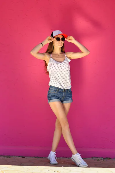 穿着嘻哈风格衣服 戴着太阳镜 在粉红墙背景下摆姿势的性感年轻女人 — 图库照片