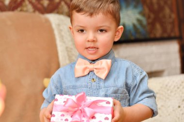 Sevimli küçük çocuk beyefendi bir mavi kot gömlek ve şeftali papyon kalpleri ve pembe bir yay ile bir güzel hediye kutusu tutar.