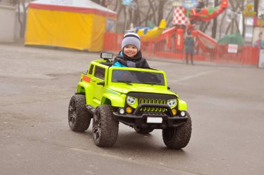 Şapkasını ve ceket şirin 2 yıl yaşlı erkek çocuk eğlence parkı yeşil elektrikli arabaya biniyor.