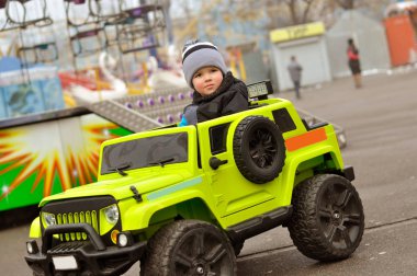 Şapkasını ve ceket şirin 2 yıl yaşlı erkek çocuk eğlence parkı yeşil elektrikli arabaya biniyor.