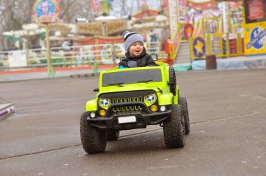 Şapkasını ve ceket şirin 2 yıl yaşlı erkek çocuk eğlence parkı yeşil elektrikli arabaya biniyor.