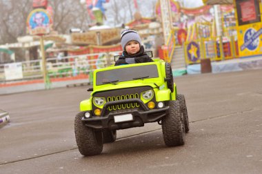 Şapkasını ve ceket şirin 2 yıl yaşlı erkek çocuk eğlence parkı yeşil elektrikli arabaya biniyor.