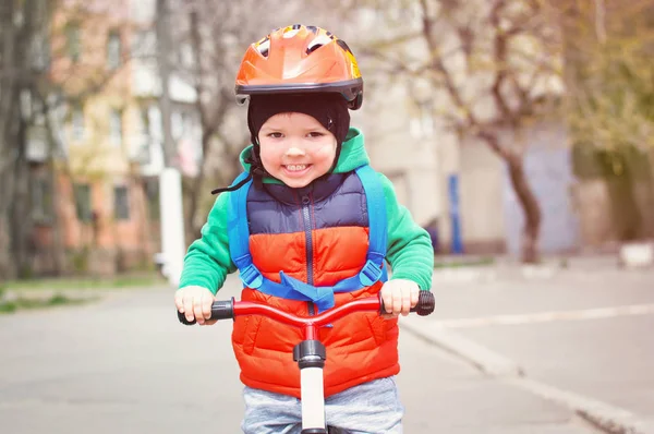 ヘルメットと背中に青いバックパックを持つ自転車に乗って赤いベストを着た小さなクールな少年 — ストック写真