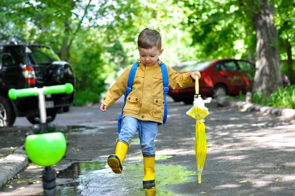 黄色のレインコートを着た小さなかわいい少年が レモンの色で傘を持って微笑みながら水たまりを歩く — ストック写真