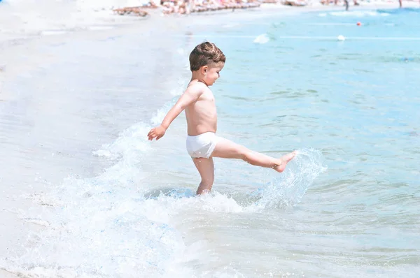 Bambino Carino Sulla Spiaggia Costume Bagno Bianco Diverte Calcia Onde — Foto Stock