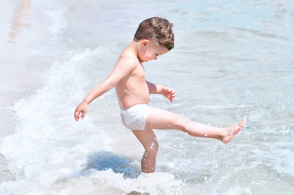 Bambino Carino Sulla Spiaggia Costume Bagno Bianco Diverte Calcia Onde — Foto Stock