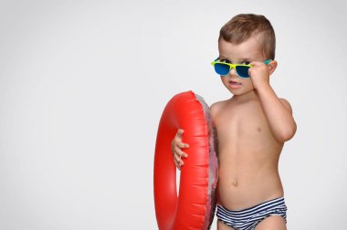 Kırmızı şişme halka ve yeşil güneş gözlüğü ile çizgili yüzme şort sevimli bir küçük çocuk.