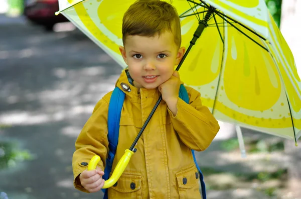 黄色のレインコートを着た小さなかわいい男の子が水たまりに立ち レモンの着色で傘を持っています — ストック写真