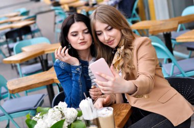 İki şık kız gülümseyen ve bir şehir kafede selfie 'ler alıyor.