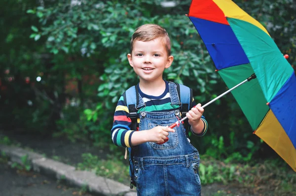 男の子でデニム全体ショートパンツ彼の多色の傘と笑顔を保持しています — ストック写真