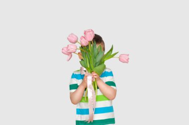 Renkli tişörtlü şirin bir çocuk elinde bir buket pembe lale tutuyor ve arkasına saklanıyor..