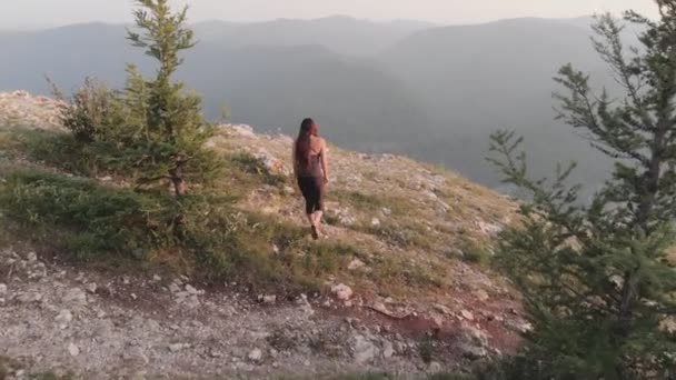 Eine junge Frau nähert sich dem Rand des Felsens und hebt freudig die Hände. — Stockvideo