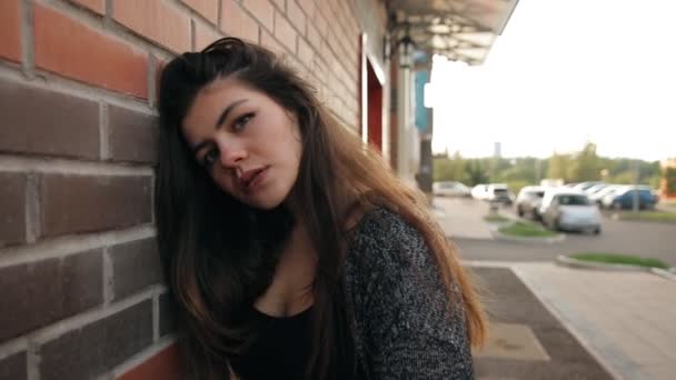 Porträtt av en ung sexig kvinna som står vid en tegelvägg som promenerar runt i staden i solnedgången. — Stockvideo