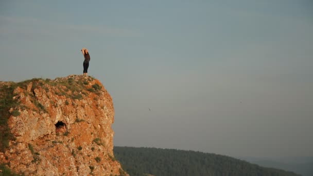 Una mujer joven se para en la cima de una montaña . — Vídeo de stock