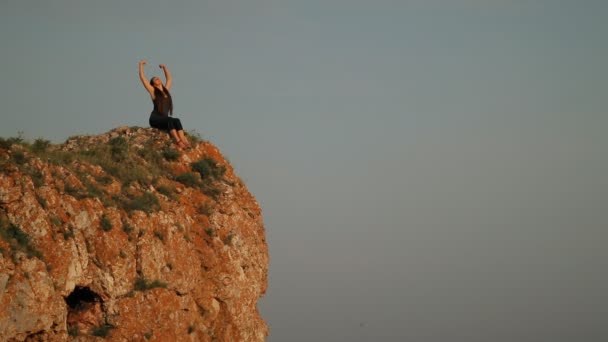 Uma jovem mulher sentada no topo de uma montanha . — Vídeo de Stock