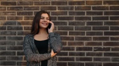Günbatımında bir tuğla duvara telefonda konuşurken gülümseyen bir çekici kadın portresi.
