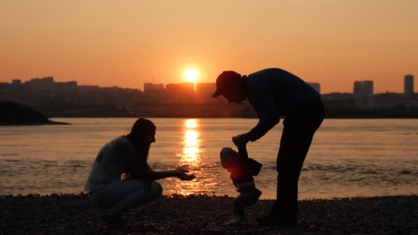 日落时一个年轻家庭在河边散步的缓慢动作. — 图库视频影像