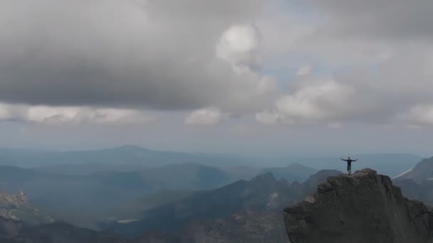 Zdjęcia lotnicze z człowieka stojącego na szczycie góry zwycięsko podnoszenia rąk i cieszyć się pięknym widokiem na dolinę. — Wideo stockowe