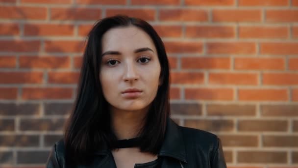 Portret van een jonge ernstige sexy vrouw tegen een bakstenen muur. Slow-motion shot. — Stockvideo