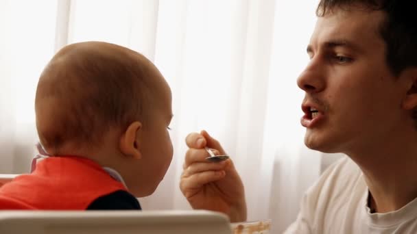 Movimento lento de um jovem pai feliz alimenta seu filho mingau de cereal . — Vídeo de Stock