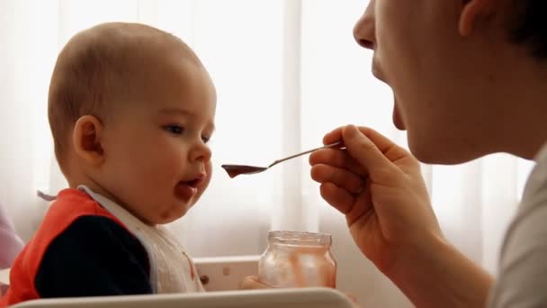 Slow motion av en ung lycklig far matar sin son baby fruktpuré. — Stockvideo