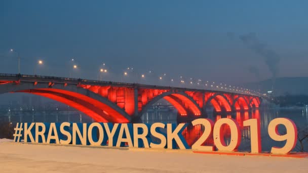 Krasnoyarsk, Oroszország - 20 Jan, 2019: jelképe a Téli Universiade 2019, a háttérben a híd Krasnoyarsk. — Stock videók