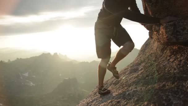 Piernas de un hombre escalando una roca al atardecer . — Vídeo de stock