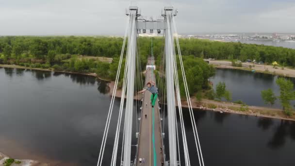 Bir adam yüksek irtifada köprünün desteği arasında gergin bir halat üzerinde yürüyor. — Stok video