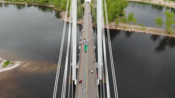 Een man loopt op een touw gespannen tussen de steunen van de brug op grote hoogte. — Stockvideo