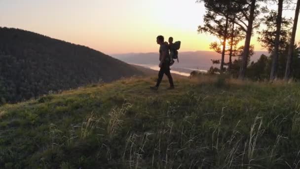 En man reser med sitt barn. Fadern visar sonen solnedgången stående på toppen av ett berg. — Stockvideo