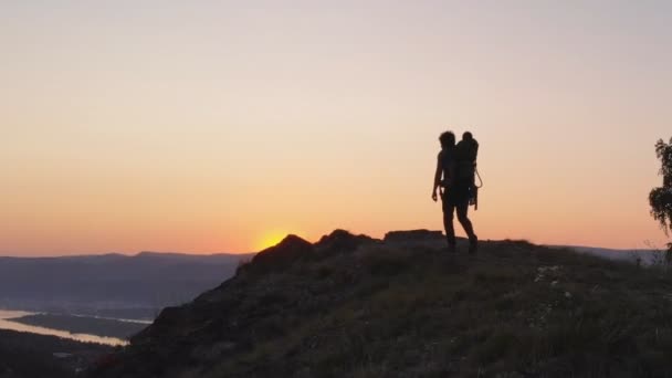 Silhouette az apja túrázás az ő kisbabája egy hegyi ösvény naplementekor. — Stock videók
