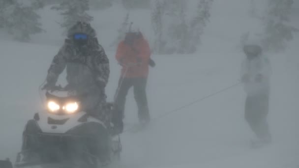 Чоловіки катаються на лижах, тримаючись за мотузку, прив'язану до снігового мотоцикла в снігопаді . — стокове відео