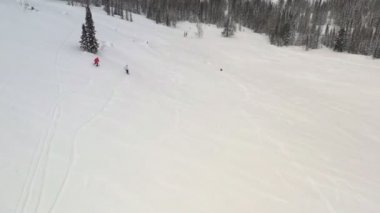 Karlı bir yamaçta uçan bir kayakçı ve snowboardcunun hava manzarası.