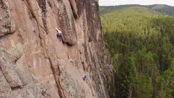 Twee mannen beklimmen een verticale granieten muur midden in een bos.. — Stockvideo