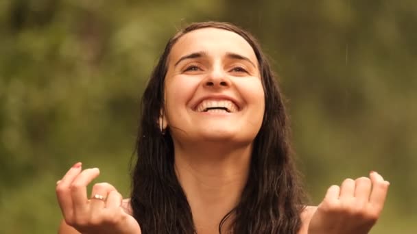 Slow motion van een jonge mooie blanke vrouw vangt graag de druppels met haar handpalmen en glimlacht terwijl ze geniet van de warme zomerregen in het bos. — Stockvideo