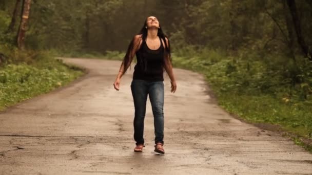 Zeitlupe einer jungen kaukasischen Frau, die den Sommerregen genießt und ihre Hände auf einer Straße im Wald hebt. — Stockvideo