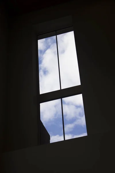 Siyah mavi bir gökyüzü ve beyaz bulutlar bakan bir pencere bölmesini silüeti