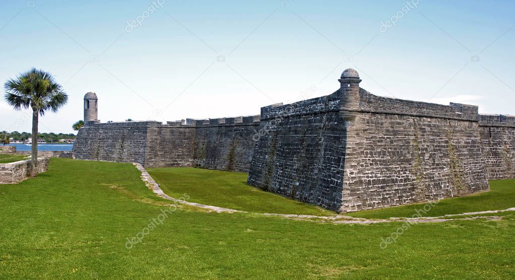 View of the Castillo de San Marcos fort, walls, towers, surrounding fields and palm trees. Saint Augustine, Florida, USA.