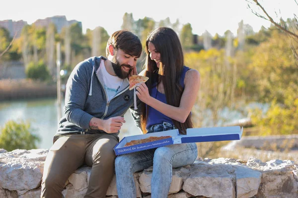 Pareja comiendo pizza al aire libre y sonriendo.Están compartiendo pizza — Foto de Stock