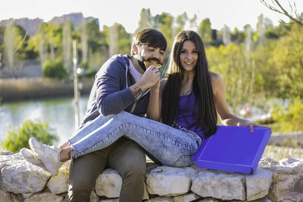 Couple eating pizza outdoors and smiling.They are sharing pizza