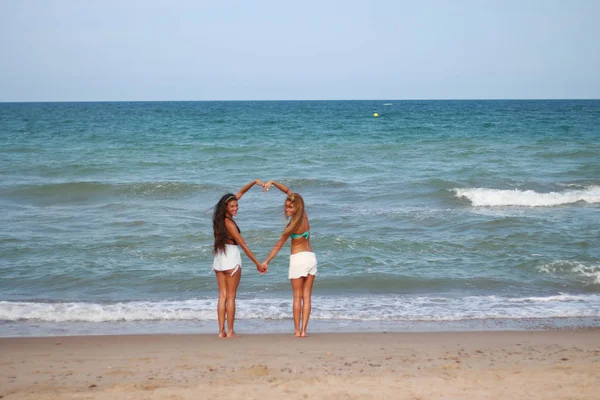 Zwei süße lustige junge Mädchen spazieren lachend am Strand entlang — Stockfoto