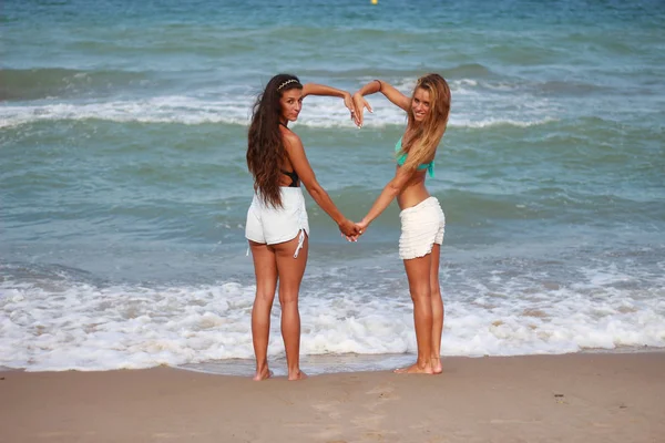 Zwei süße lustige junge Mädchen spazieren lachend am Strand entlang — Stockfoto