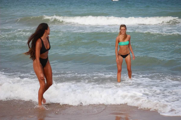 Две милые юные девушки прогуливаются по пляжу, смеясь — стоковое фото