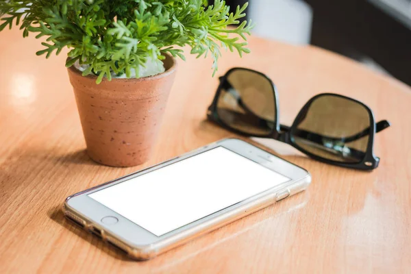 Mobile phones and sunglasses, travel accessories, mobile phones and glasses on wooden boards. There is a small potted plant next to it.