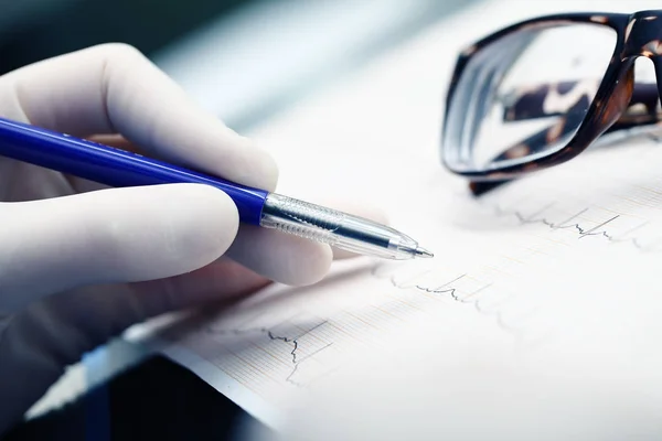 Arzt liest Ecg und macht mit Stift und Glas Spuren auf dem Papier — Stockfoto