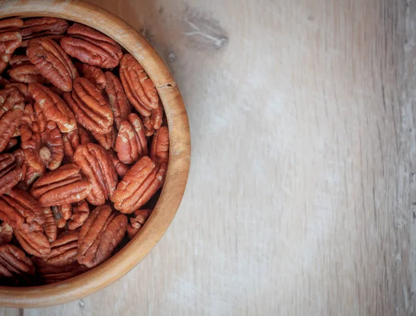 wooden bowl with pecan nuts on wooden table, delicious nuts, flat lay