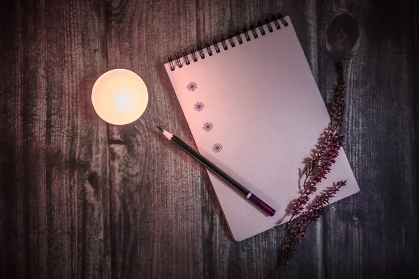romantic list on vintage notebook with bright candle, pencil and purple flower, wish list